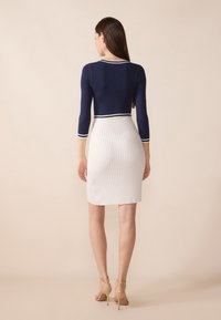 Haut ajusté marine avec des accents à rayures blanches, associé à une jupe crayon blanche à côtes, longueur au-dessus du genou, complété par des sandales à talons nus.