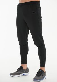 Sorte træningsbukser lavet af letvægtsmateriale, med slim fit, elastisk talje og reflekterende detaljer på nederste ben.