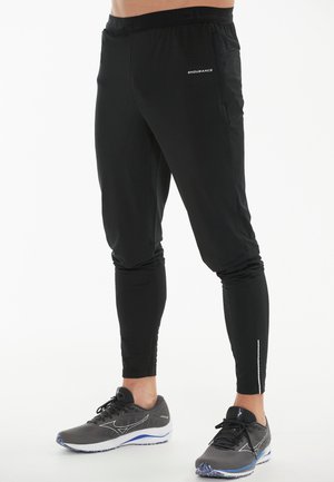 Zwarte sportbroek van lichtgewicht materiaal, met een slim fit, elastische tailleband en reflecterende accenten op de onderbenen.