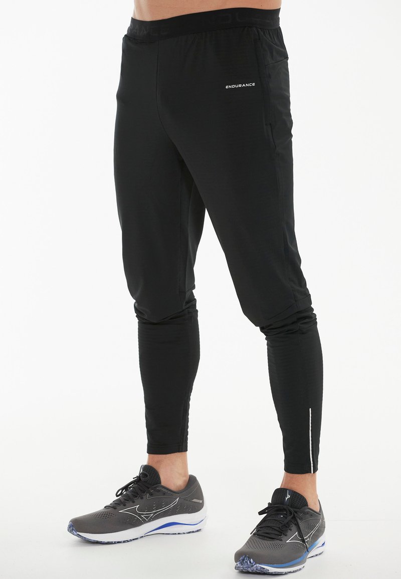 Sorte træningsbukser lavet af letvægtsmateriale, med slim fit, elastisk talje og reflekterende detaljer på nederste ben.