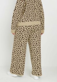 Leopardmönstrade vida byxor i beige och brunt stickat tyg; elastisk midja och ribbade manschetter; matchas med vita sneakers.