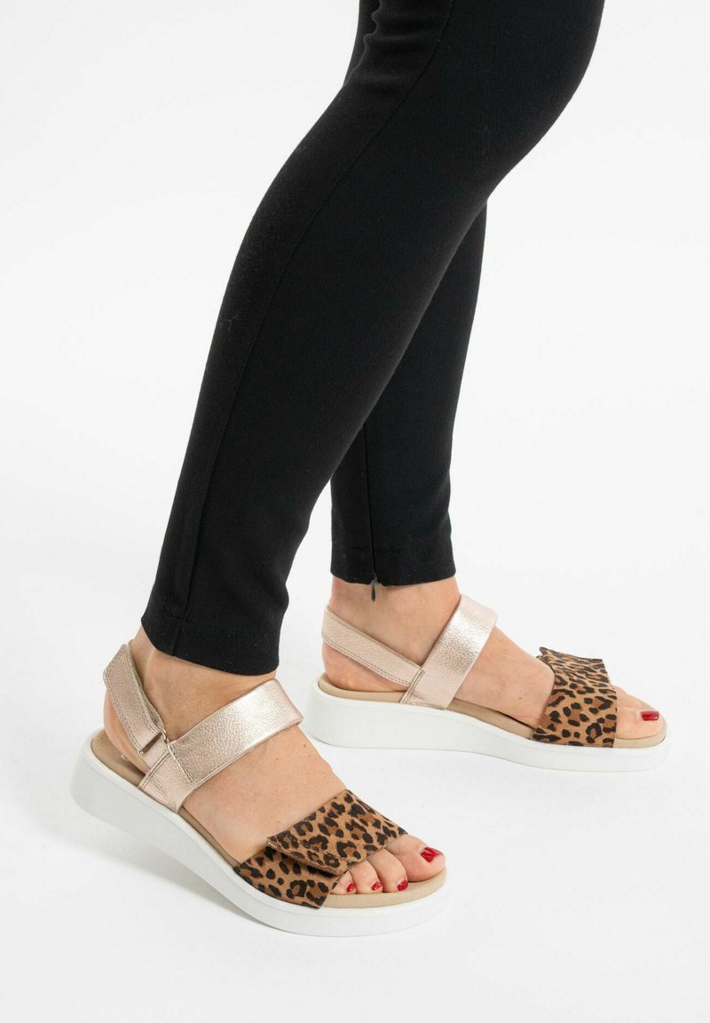 Sandály s leopardím potiskem a kovovými růžově zlatými popruhy, s širokou stélkou a bílou gumovou podrážkou, odhalující prsty a klenbu.