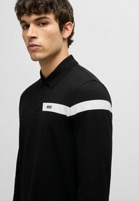 Schwarzes Langarm-Polohemd mit einem weißen Horizontalstreifen und dem "BOSS"-Logo auf der Brust. Strukturierter Stoff und design mit Knopfkragen.