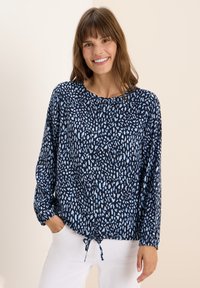Blusa a maniche lunghe color blu navy con motivi e designs astratti in azzurro chiaro, orlo arricciato con un laccio regolabile. Tessuto leggero.