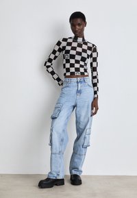 Black and white checkered long-sleeve top with graphic details, paired with light blue cargo jeans featuring flap pockets and black platform boots.
