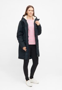 Svart isolerad jacka med en huva kragen av faux päls, framfickor och dragkedja. Under, en rosa och vit randig tröja. Svarta tajta jeans.