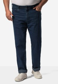 Tmavě modré džíny s rovnými nohavicemi, s poutky na opasek a ohrnutými manžetami, v kombinaci s bílými sportovními teniskami.