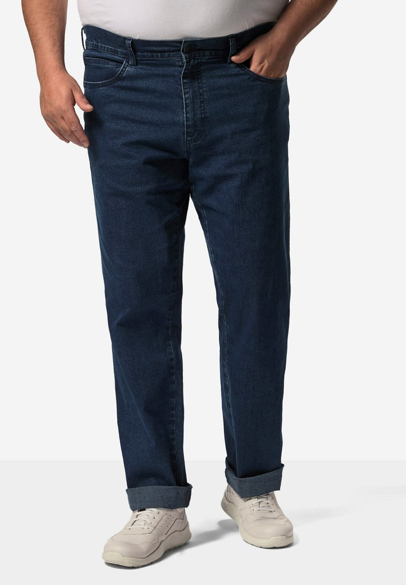 Tmavě modré džíny s rovnými nohavicemi, s poutky na opasek a ohrnutými manžetami, v kombinaci s bílými sportovními teniskami.