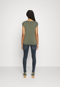Top a maniche corte verde oliva, taglio aderente, abbinato a jeans skinny scuri e sneaker alte verdi con dettagli in bianco e nero.