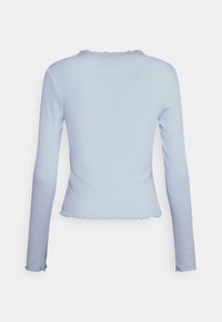 Ljusblå långärmad topp, ribbad textur, rund halsringning, kortad fåll med scallopkanter, sömlös konstruktion, inga synliga knäppningar.