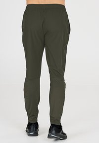 Dunkelgrüne Sporthose mit elastischem Bund und Seitentaschen, mit einem schlichten Design und schmalem Schnitt, kombiniert mit schwarzen Sneakers.