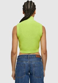 Suéter sin mangas cortado en un vibrante color verde lima de punto. Presenta un cuello alto y una textura acanalada, combinado con unos jeans de denim azul.