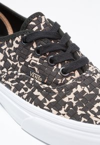 Tenisky z černé a béžové tkané látky s černými šňůrkami, gumovou podrážkou a logem Vans. Obsahují texturovaný vzor a kulatou špičku.