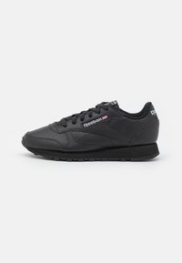 Baskets Reebok noires avec une tige en cuir lisse, un bout arrondi, un col rembourré et une semelle en caoutchouc plate. Elles présentent une fermeture à lacets et des accents de logo.