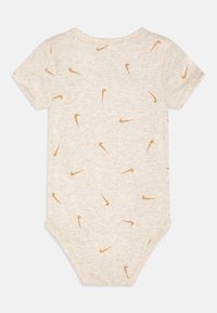 Body à manches courtes beige en tissu doux, orné de logos Nike en forme de swoosh orange dispersés dans un motif répétitif.
