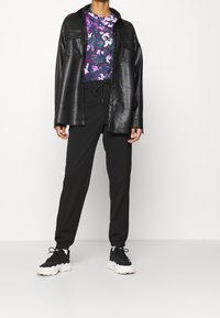 Svart skinnskjorta med tryckknappar över en lila blommig topp. Svarta joggerbyxor och svarta sneakers med vita sulor.