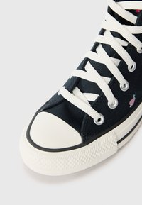 Schwarzer Canvas-Sneaker mit weißen Schnürsenkeln und Gummikappe. Verfügt über pinke und grüne Akzente an der Seite sowie eine strukturierte weiße Gummisohle.