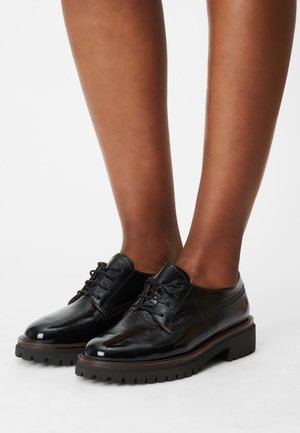 Black leather lace-up shoes with a textured surface, round toe, and thick, ridged rubber sole. Detailed stitching visible along the edges.