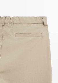 Pantalon beige avec une taille élastique, passants de ceinture et une poche passepoilée à l'arrière.