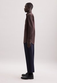 Bruine blouse met lange mouwen en knoopmanchetten, gestyled met marineblauwe wijde broek en zwarte schoenen. Glad materiaal; aansluitend ontwerp; enkele borstzak.