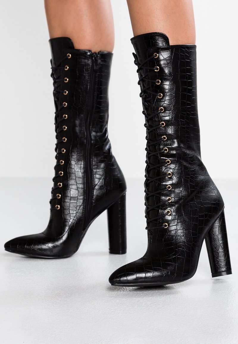 Bottes à talons hauts noires en cuir embossé croco, avec bout pointu, lacets à l'avant, œillets dorés et détail de fermeture éclair latérale.