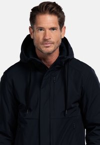 Marine waterdichte jas met hoge kraag en verstelbare capuchon, voorzien van ritssluitingen en een gladde, gestructureerde stof.