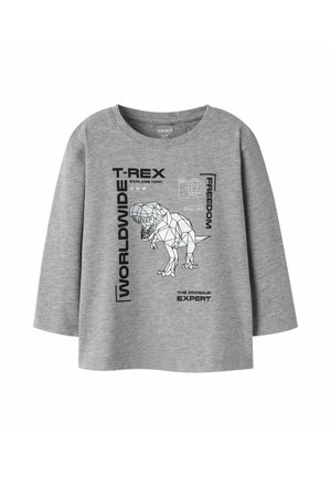 Chemise grise à manches longues avec un motif géométrique de T-Rex et un texte noir disant "MONDIAL," "T-REX," "LIBERTÉ," et "L'EXPERT DU DINOSAURE".