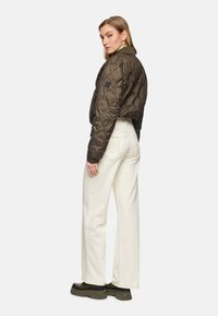 Brown quilted jacket with a cropped design, paired with high-waisted white wide-leg pants. Black accent on the jacket's arm. Smooth texture.