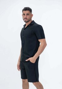 Chemise noire à manches courtes avec un col boutonné, dotée d'une poche poitrine, associée à un short noir assorti. Tissu texturé.