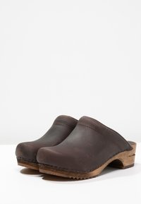 Bruna läderträsprickor med rund tå, slät yta och trä sål; presenterade från en sidovy som visar design och konstruktionsdetaljer.