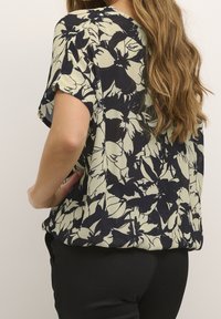 Korte mouwblouse in een crèmekleurig en marineblauw bloemenpatroon, met een relaxte pasvorm en lichtgewicht textuurstof.