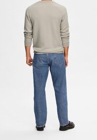 Camisa de manga larga gris claro combinada con jeans de denim azul. Los jeans tienen un corte clásico y dos bolsillos traseros. Unos zapatos negros completan el atuendo.