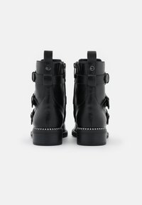 Botas de cuero negro hasta el tobillo con puntera redonda, dos correas laterales y tachuelas plateadas a lo largo de la suela, con un pequeño tacón y cierre de cremallera.