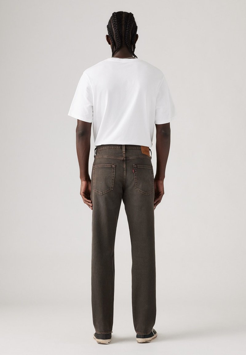 Braune gerade geschnittene Jeans mit einem Lederpatch am Rücken, großen hinteren Taschen und einem weißen kurzärmeligen T-Shirt, das von hinten getragen wird.