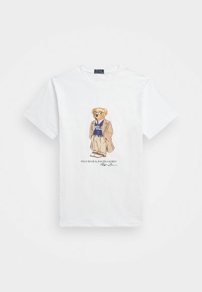Bela bombažna majica s kratkimi rokavi, ki prikazuje risanega medveda v sončnih očalih, oblečenega v blazer in vijolično pulover s napisom "Polo". Pod obliko je podpis.