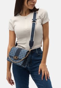 Blue patterned crossbody bag with a gold chain accent, featuring a smooth leather strap and a rectangular shape.
