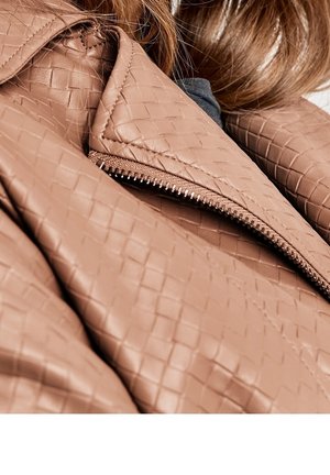 Close-up of a person wearing a brown woven-texture leather jacket with a visible metal zipper and light brown hair.