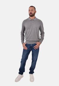 Polo grigia a maniche lunghe con colletto e bottoni, abbinata a jeans blu scuro e sneaker bianche. Design semplice con polsini a coste.