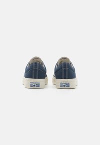 Mornarske platnene tenisice s bijelim gumenim đonom, kontrastnim šavovima i plavim "CONVERSE ALL STAR" brendiranjem na peti. Niska dizajna.