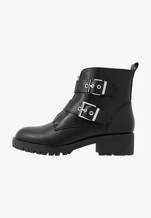 Mustad musta nahast ankle boots, millel on kaks hõbedast messingist rihma, tekstureeritud pind, raskemeelne konts ja jäik tall.