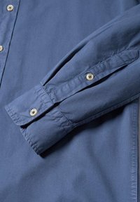 Manche longue d'une chemise bleue à boutons avec des boutons visibles de couleur claire au poignet et sur la patte de manche.