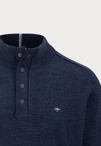 Pullover a maglia blu navy con colletto alto, placket con tre bottoni e piccolo logo ricamato sul petto. Tessuto strutturato.