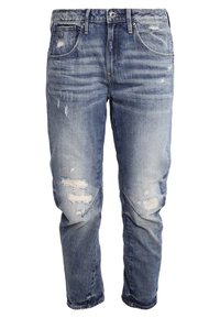Jeans en denim bleu délavé avec des patchs déchirés et des détails de whiskering, coupe droite, style cinq poches et fermeture à bouton.