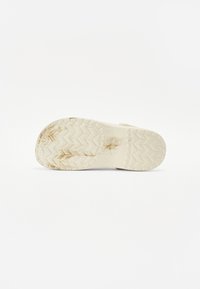 White rubber shoe sole with zigzag tread pattern. Slightly dirty, showing wear. Features a smooth, matte texture and rounded edges.