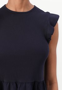 Dunkelblaues Kleid mit geripptem Textur; taillierter Oberteil und geraffte Flügelärmel; fließender Rock mit gerafftem Saum.