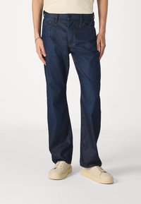 Jeans de mezclilla azul oscuro con un diseño de pierna recta, que cuentan con un estilo clásico de cinco bolsillos y un cierre de botón estándar.
