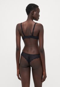 Reggiseno in pizzo nero e perizoma abbinato. Il reggiseno ha spalline regolabili e chiusura a gancio. Il perizoma presenta bordi in pizzo scallop.