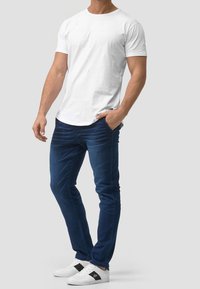 White short-sleeve t-shirt paired with dark blue slim-fit jeans and white sneakers with black accents. Smooth fabric, casual design.
