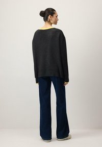 Pull oversize gris foncé avec détail jaune au niveau du col, associé à un pantalon ample bleu marine. Le tissu semble doux, avec une coupe décontractée.
