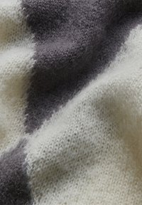 Weiche Strickdecke mit abwechselnden hellen Creme- und dunklen Graustreifen, mit einem flauschigen Textur und einem gemütlichen Aussehen.